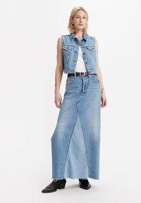 Denim vest met een cropped ontwerp, gecombineerd met een lange denim rok met een voornaad en een rafelige zoom. Een zwarte riem en enkerschoenen maken de look compleet.