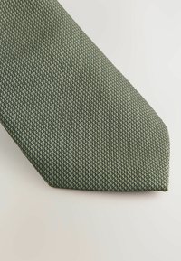Grüne Krawatte mit einem strukturierten Muster und kleinen geometrischen Designs. Die Krawatte hat eine spitze Spitze und eine glatte Oberfläche.