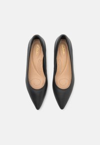 Sorte skinn, spisse ballettsko med polstret såle, med perforert design og preget gull "Clarks" logo.