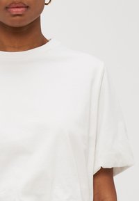 White cotton T-shirt with a round neckline and short sleeves. Features a smooth texture and relaxed fit with no visible patterns or accents.