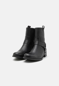 Botines de cuero negro con una textura suave, una correa lateral con acentos metálicos y un pequeño tacón apilado. Cuenta con una pestaña para facilitar su uso.