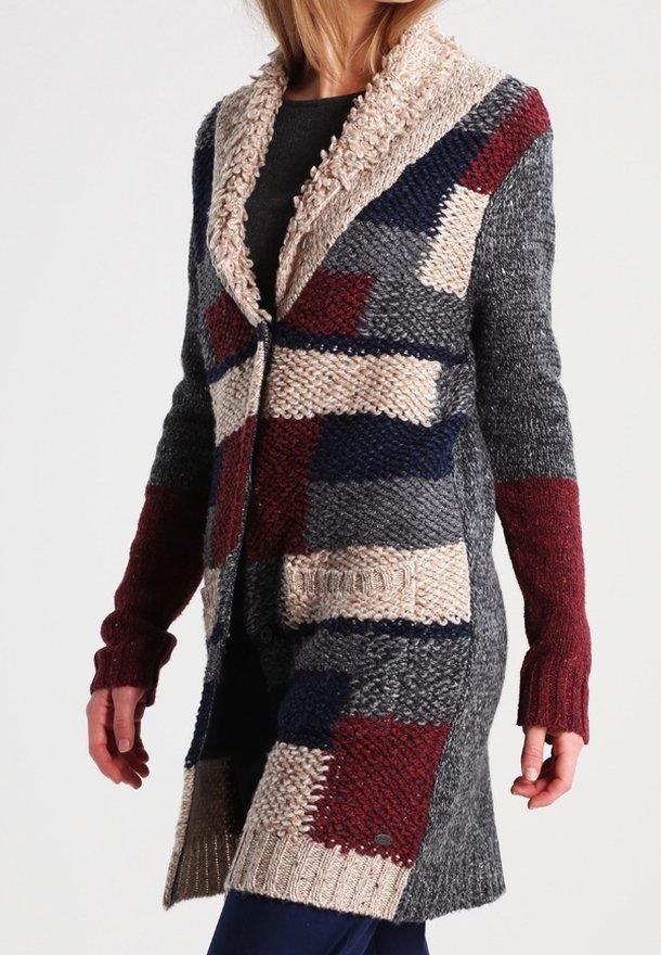 Femme portant un cardigan en tricot multicolore avec un grand col châle, des poches plaquées et des manches longues dans des nuances de gris, bordeaux, marine et beige.