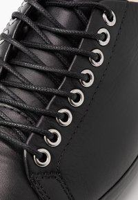 Čierny kožený zvršok topánok s plochými čiernymi šnúrkami prevlečenými cez strieborné očká; hladká textúra, zaoblený špička a zosilnené švy.