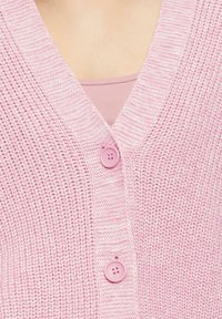 Helles pinkes Strickcardigan mit V-Ausschnitt, ausgestattet mit zwei passenden Knöpfen und einer strukturierten Webart. Über einem hellen pinken Oberteil getragen.