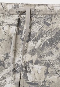 Zbliżenie na szare i beżowe spodenki w kamuflaż z przednim ściągaczem w pasie i widocznymi detalami szwów.