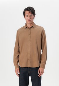 Chemise marron à boutonner en tissu doux, avec un col classique, des boutons à l'avant et des manches longues, associée à un jean en denim noir.