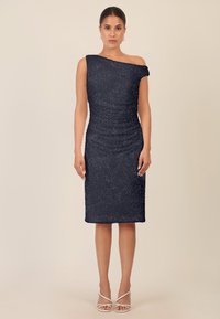 Granatowa sukienka na jedno ramię z teksturowanej tkaniny i detalami marszczenia. Sukienka o długości do kolan z dopasowanym krojem, zestawiona z sandałami na paski.