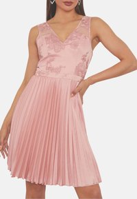 Rosa plisserad klänning med V-ringning och blommöster broderi på genomskinliga axelband. Slät textur med flödande plisseringar, längd ovanför knä.