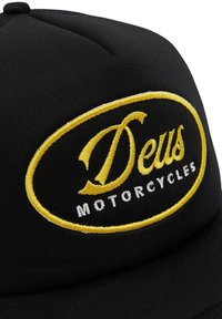 Schwarze Stoffmütze mit einem gestickten ovalen Logo, das "Deus" in gelber Schrift und "MOTORCYCLES" in weißem Text zeigt. Glatte Textur.