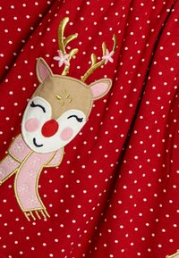 Röd tyg med vita prickar som har en broderad ren med gyllene horn, rosa halsduk och leende ansiktsdetaljer.