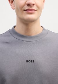 Hallhallane sviiter ribidega kaelusega ja väike must "BOSS" logo esiosas. Sile tekstuur, klassikaline lõike disain.