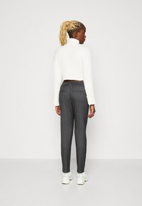 Un col roulé blanc à côtes, au design cropped, associé à un pantalon gris à rayures. Le mannequin porte des baskets blanches, au toucher lisse et à la coupe ajustée.