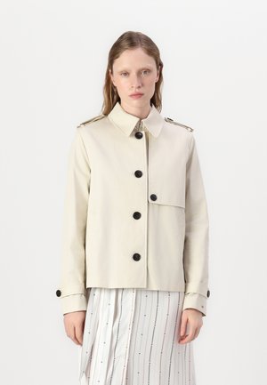 Beige katoenen jack met een kraag, vijf zwarte knopen en epauletten. Gladde textuur, cropped ontwerp en geen zichtbare zakken.