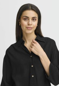 Camicia in lino nera con colletto, chiusura frontale a cinque bottoni e maniche ampie. Morbido al tatto con sottili linee orizzontali.