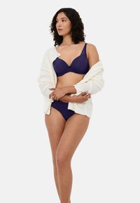 Laivastonsininen rintaliivit ja niihin sopivat bikinihousut, joissa on sileä kangas, hienostunut pitsireunus ja valkoinen, kuvioitu neuletakki, joka on vedetty hartioiden yli.