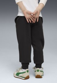 Zwarte joggingbroek met elastische boorden, zakken, gecombineerd met witte en groene sneakers met een textuurzool en suède accenten.
