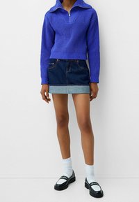 Pull-over en maille bleu roi avec col zippé, associé à une mini-jupe en denim foncé avec un ourlet en denim clair. Mocassins noirs et chaussettes blanches.