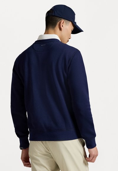 Navyblauwe sweatshirt van zachte stof met een ronde halslijn en geribde mouwen. G gedragen over een wit overhemd met kraag, wat een casual stijl laat zien.