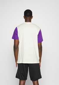 Camiseta de manga corta con un cuerpo color crema y mangas moradas, hecha de un tejido suave. Combinada con pantalones cortos negros y un corte relajado.