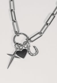 Silver chain necklace featuring charms: a star, a black heart, and a horseshoe with rhinestones, showcasing mixed shapes and textures.