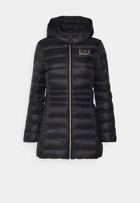 Svart vadderad jacka med dragkedja framtill, huva och logotypdetalj. Har ett lätt, glansigt material med sydd quiltad design.