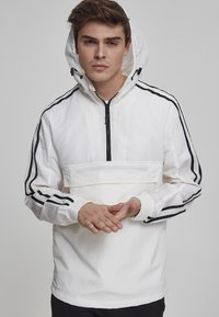 Fehér zipzáras pulóverdzseki fekete oldalsávokkal, kapuccnival és rugalmas mandzsettákkal, elülső zsebbel és könnyű, texturált anyagból készült.