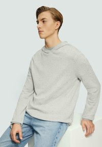 Lichtgrijze sweatshirt met een gestructureerde textuur, capuchon, relaxte pasvorm en lange mouwen. Gecombineerd met lichtblauwe jeans.