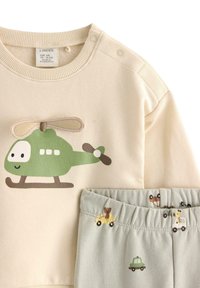 Beżowa bluza z grafiką zielonego helikoptera; zielone elastyczne spodnie z małymi wzorami zwierząt i pojazdów. Miękki bawełniany materiał.