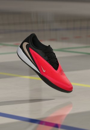 Sportschuh in Rot und Schwarz mit Nike-Logos, der über einem Hallenboden mit farbigen Linien schwebt.