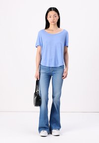 Un tricou scurt de culoare bleu deschis, cu un croi lejer, asociat cu blugi evazați de culoare bleu deschis. O geantă de mână neagră cu un design texturat și adidași albi.