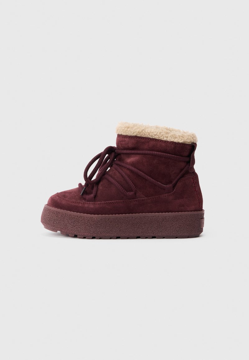 Stivale alla caviglia in suede bordeaux con colletto in pelliccia sintetica, chiusura con lacci e suola in gomma texturizzata con una piattaforma spessa.