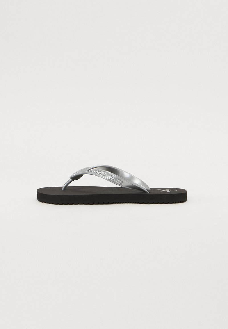 Sølvrutete flip-flopsandal med en teksturert svart gummisåle. Har en blank stropp og preget logo detaljering på stroppen.