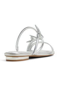 Silver metallic sandal with butterfly accents, thin straps, and a small block heel featuring a decorative gold band at the base.