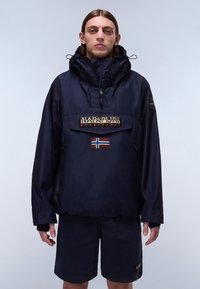 Chaqueta de pullover azul marino con un bolsillo frontal, que presenta un logo de la marca y un parche de la bandera noruega. Fabricada con un material suave e impermeable.