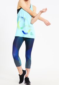 Débardeur sans manches bleu clair avec un design graphique, associé à des leggings bleus dégradés comportant des motifs géométriques et une silhouette ajustée. Baskets noires.