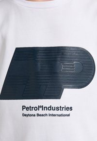 Witte sweatshirt met een verhoogd, donkerblauw logo met lijnen en de tekst "Petrol® Industries Daytona Beach International."