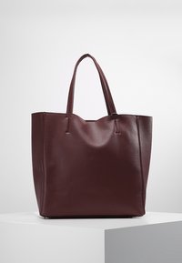 Sac fourre-tout en cuir bordeaux avec deux poignées robustes, forme rectangulaire, surface texturée et design minimaliste.
