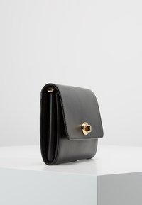 Czarny skórzany portfel z klapą i złotymi akcentami. Kompaktowa konstrukcja z wyraźnymi liniami i gładką teksturą. Brak widocznych wzorów lub akcentów.