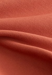 Gestructureerde stof in koraalkleur, met een glad, licht rekbaar oppervlak, diagonale geweven patronen en zachte plooien.