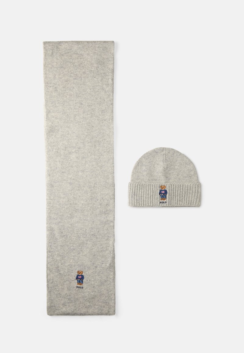 Conjunto de cachecol e gorro cinza em malha, feito de material suave. O cachecol é longo e plano; o gorro tem um punho canelado com um logótipo de urso bordado na frente.