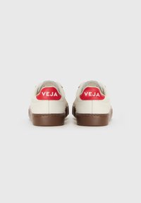 Hvit sneaker med brun såle, med rødt logo på hælen og grå detaljer. Myk tekstur med et rent, minimalistisk design.