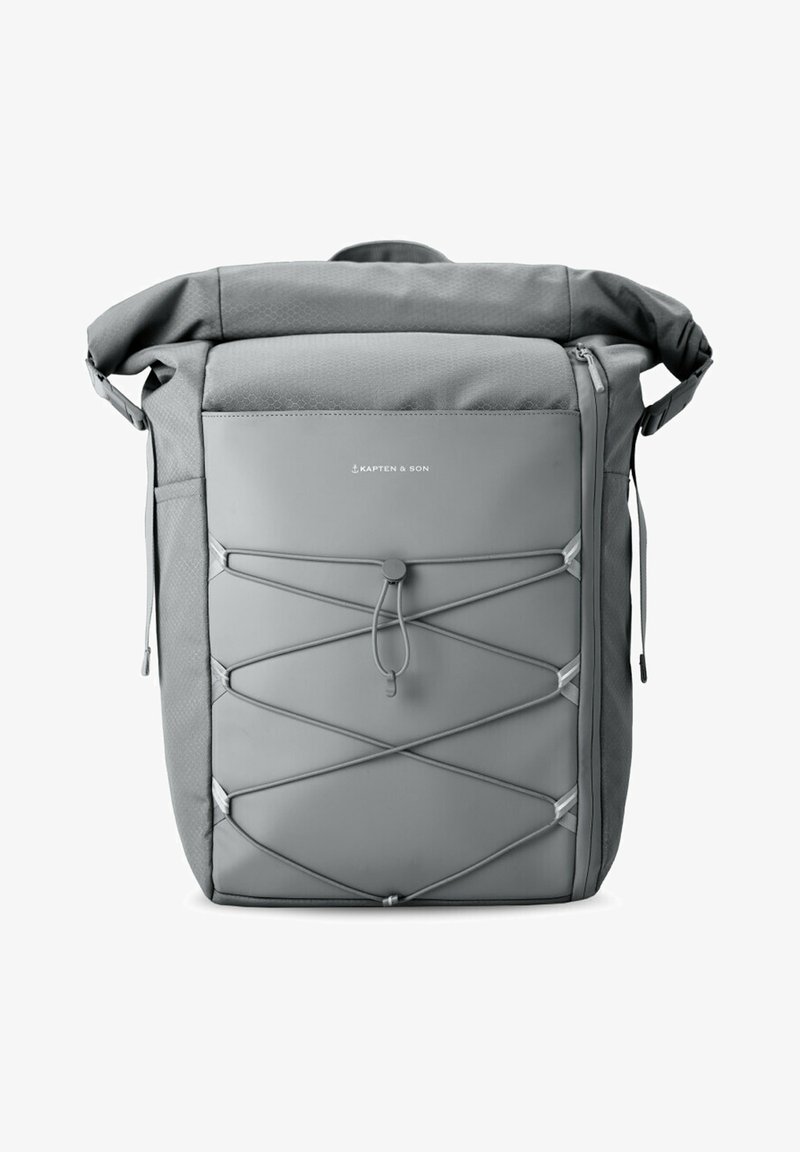 Sac à dos gris avec un design à rabat, fabriqué en tissu durable. Présente un détail en corde élastique à l'avant et des poches zippées sur les côtés.