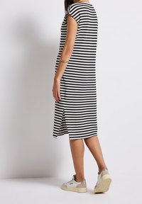 Randig midiklänning i svart och krämfärg, med ärmlösa axlar, sidospjälor och ribbad textur. Kombinerad med vita sneakers.