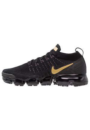 Černý teniska Nike Vapormax Flyknit se zlatým logem Swoosh, pleteným svrškem a segmentovanou podrážkou s vzduchovým polštářem.