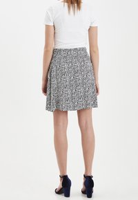 Gonna floreale in bianco e nero con design svasato, vita elastica e tessuto leggero. Indossata con sandali alti blu navy.