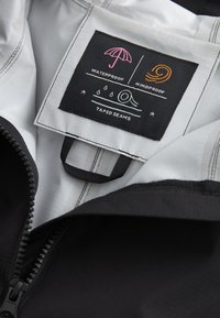 Black waterproof jacket interior features a care label with icons for waterproof, windproof, and taped seams on a white background.