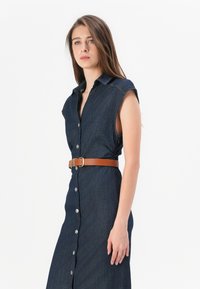 Denimkjole med korte ermer, knapper foran og et brunt belte i midjen. Mørkeblått stoff med subtil tekstur og en tettsittende silhuett.