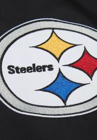 Schwarzer Stoff mit einem bestickten Logo, das drei Diamanten in Gelb, Rot und Blau zeigt, eingefasst von einem silbernen Rand mit dem Wort "Steelers."