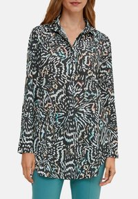 Chemise à manches longues en tissu noir avec un motif abstrait coloré, dotée d'un col et d'une fermeture à boutons. La surface texturée ajoute de l'intérêt visuel.