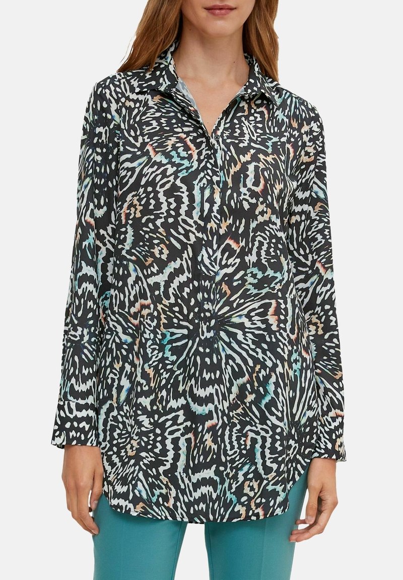Chemise à manches longues en tissu noir avec un motif abstrait coloré, dotée d'un col et d'une fermeture à boutons. La surface texturée ajoute de l'intérêt visuel.